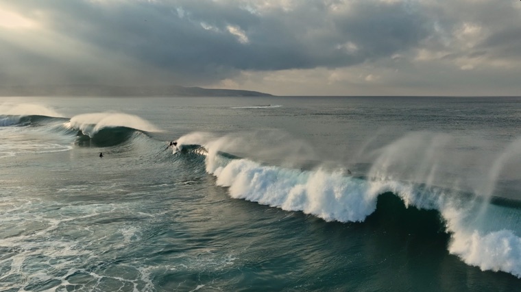 Surfers riding a breaking wave at dawn